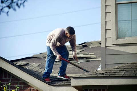 A roofer tearing off old shingles ahead of a full roof replacement